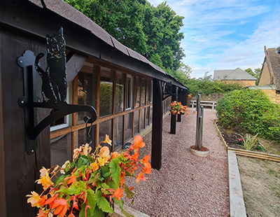 exterior view of a building with flower baskets and a cat silhouette decoration surrounded by greenery and a clear blue sky featuring twenty nine outdoor flowers in bloom