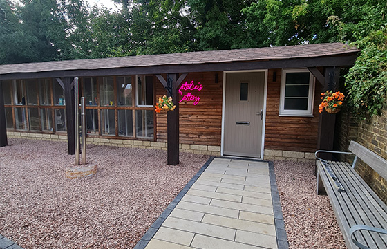 a wooden cabin with large windows and a lighted sign that reads atelies attic surrounded by flowering plants and a stone walkway with a bench perfect for a cozy retreat or getaway six charming details